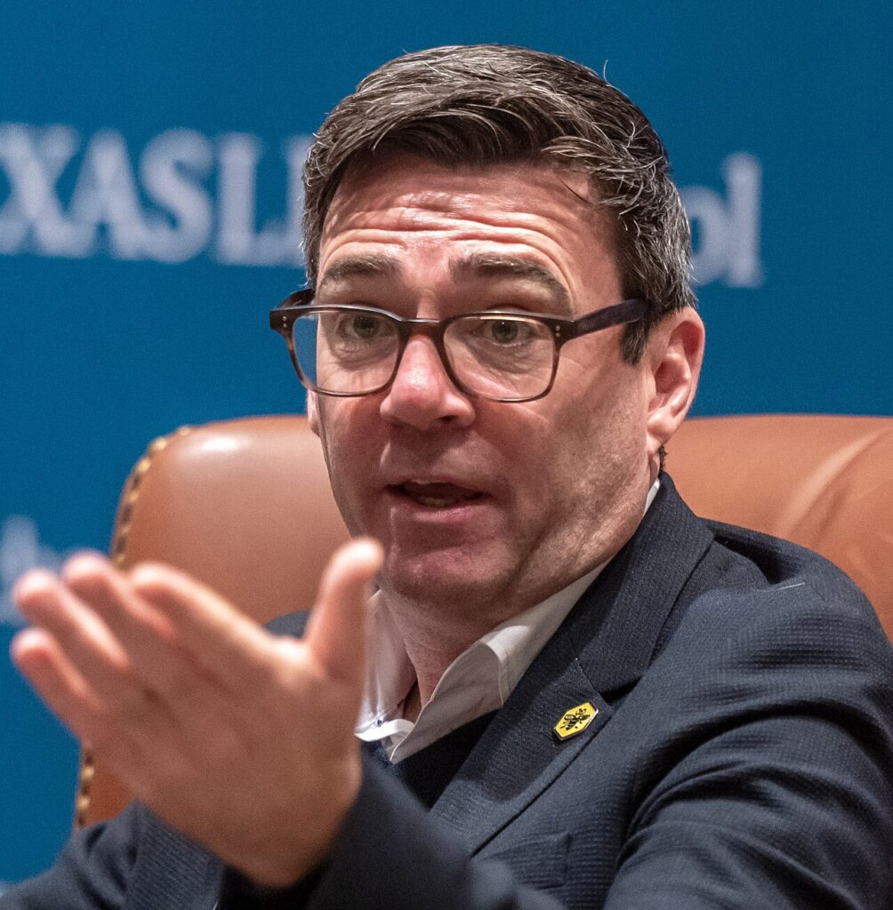 Andy Burnham looking slightly off to the side with his hand gesturing upward.